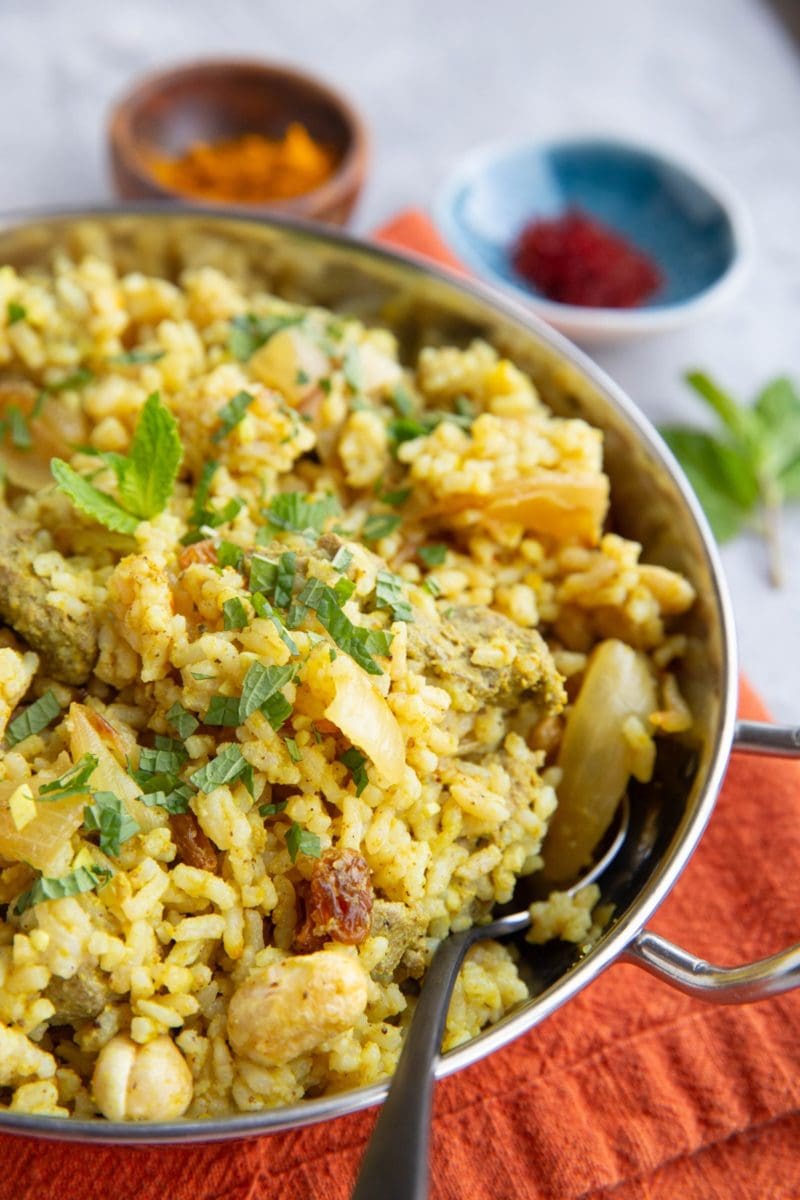 Stainless steel dish full of lamb biryani sprinkled with fresh mint. Ready to serve.