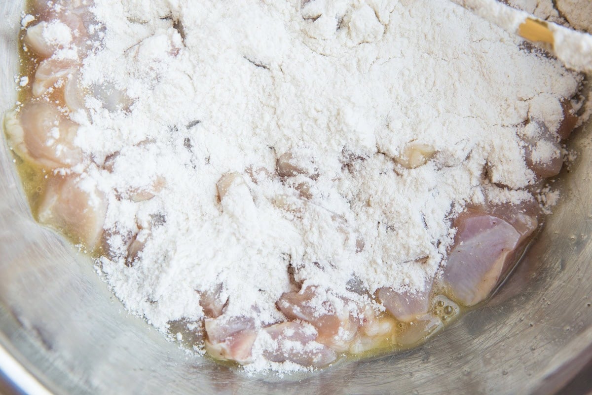Chicken pieces coated with egg with flour on top, ready to be tossed together to coat the chicken in flour for breading.