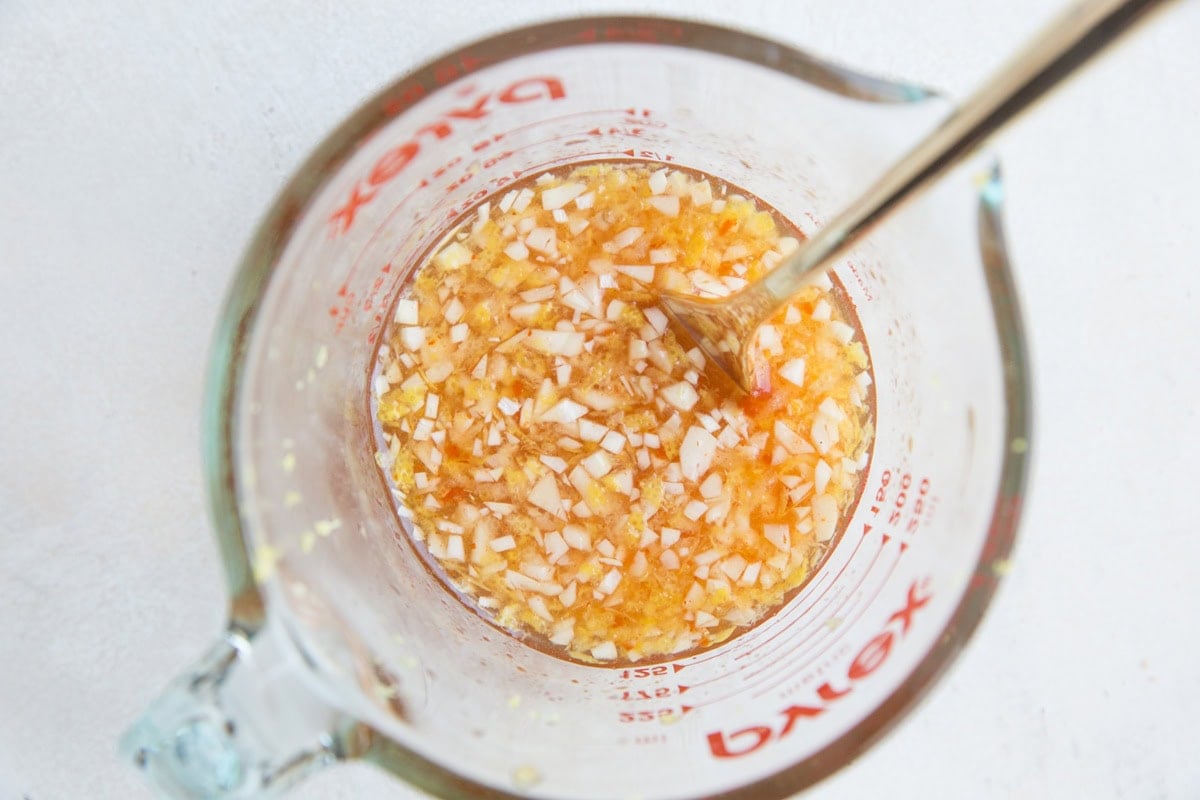 Lemon sauce in a measuring cup with fresh garlic to make lemon chicken