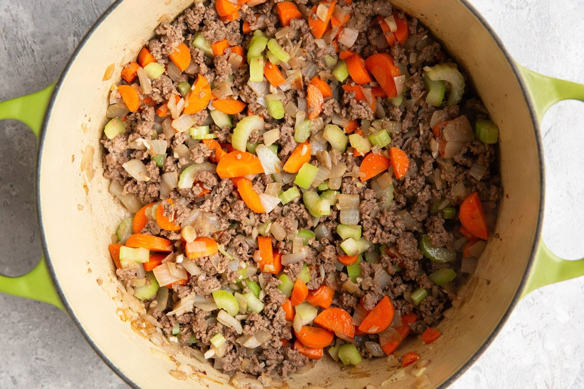 Large pot with onion, ground beef, celery, and carrots cooking.