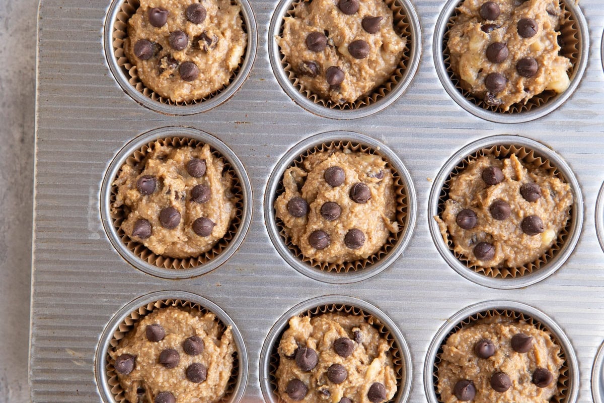 Muffin tray full of banana muffin batter with chocolate chips on top.