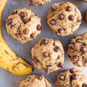Banana peanut butter muffins sitting on a backdrop with a ripe banana to the side.