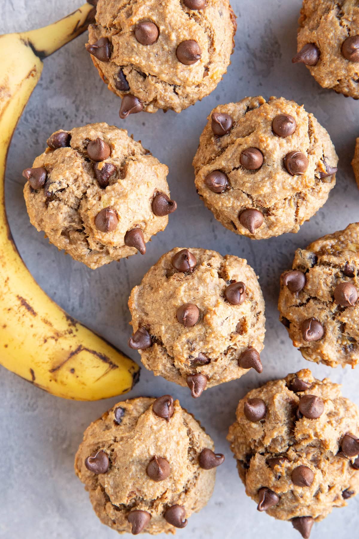Banana peanut butter muffins sitting on a backdrop with a ripe banana to the side.