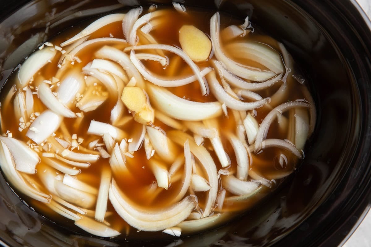 Slow cooker full of broth, onions, garlic, and ginger to make ramen broth.