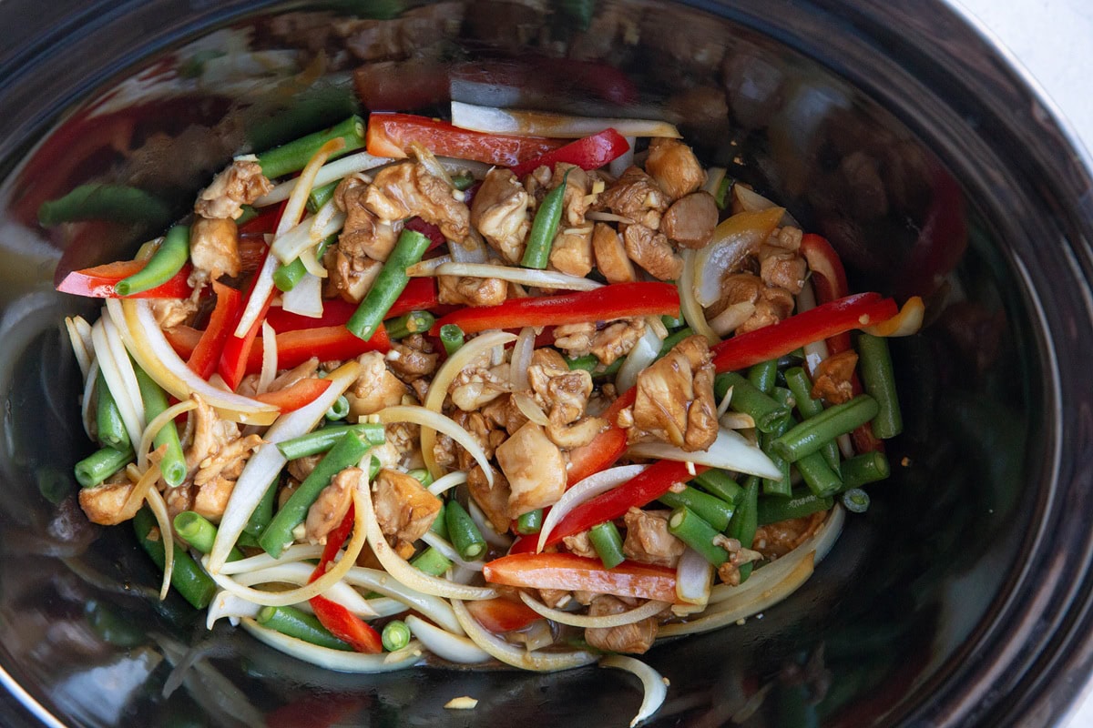 Slow cooker full of chopped chicken, teriyaki sauce, bell pepper, and green beans.