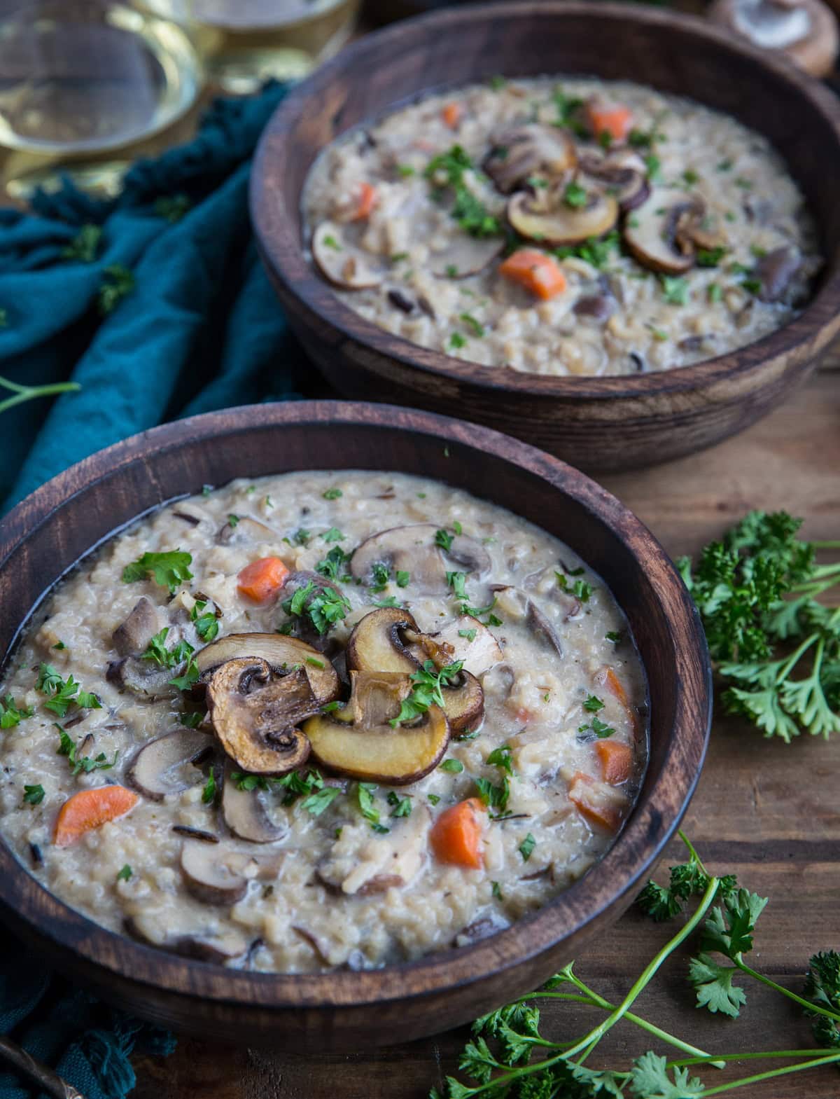 Two wooden bowls full of creamy mushroom soup with fresh parsley to the side and a blue napkin in the background.