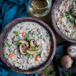 Creamy vegan mushroom soup in two wooden bowls with fresh parsley sprinkled on top and two glasses of wine to the side.