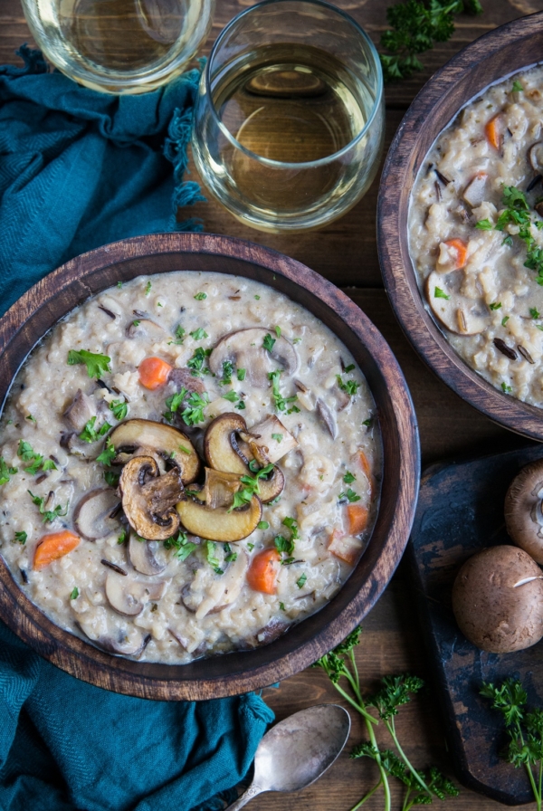 Creamy vegan mushroom soup in two wooden bowls with fresh parsley sprinkled on top and two glasses of wine to the side.