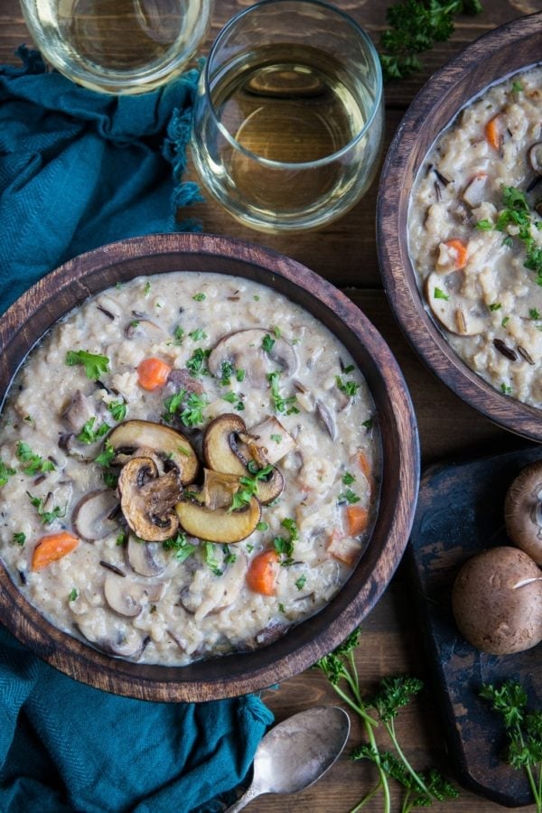 Creamy vegan mushroom soup in two wooden bowls with fresh parsley sprinkled on top and two glasses of wine to the side.
