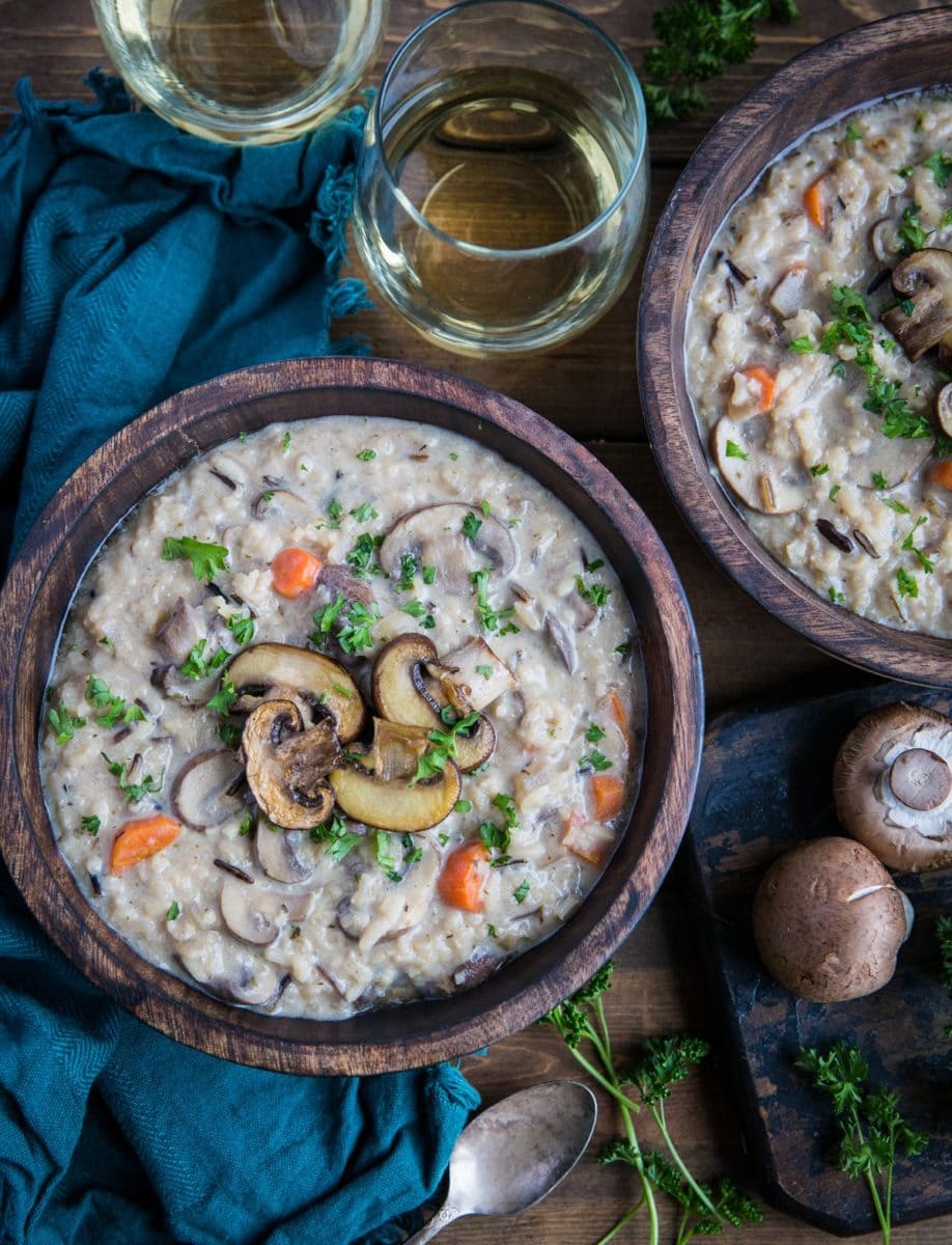Creamy vegan mushroom soup in two wooden bowls with fresh parsley sprinkled on top and two glasses of wine to the side.