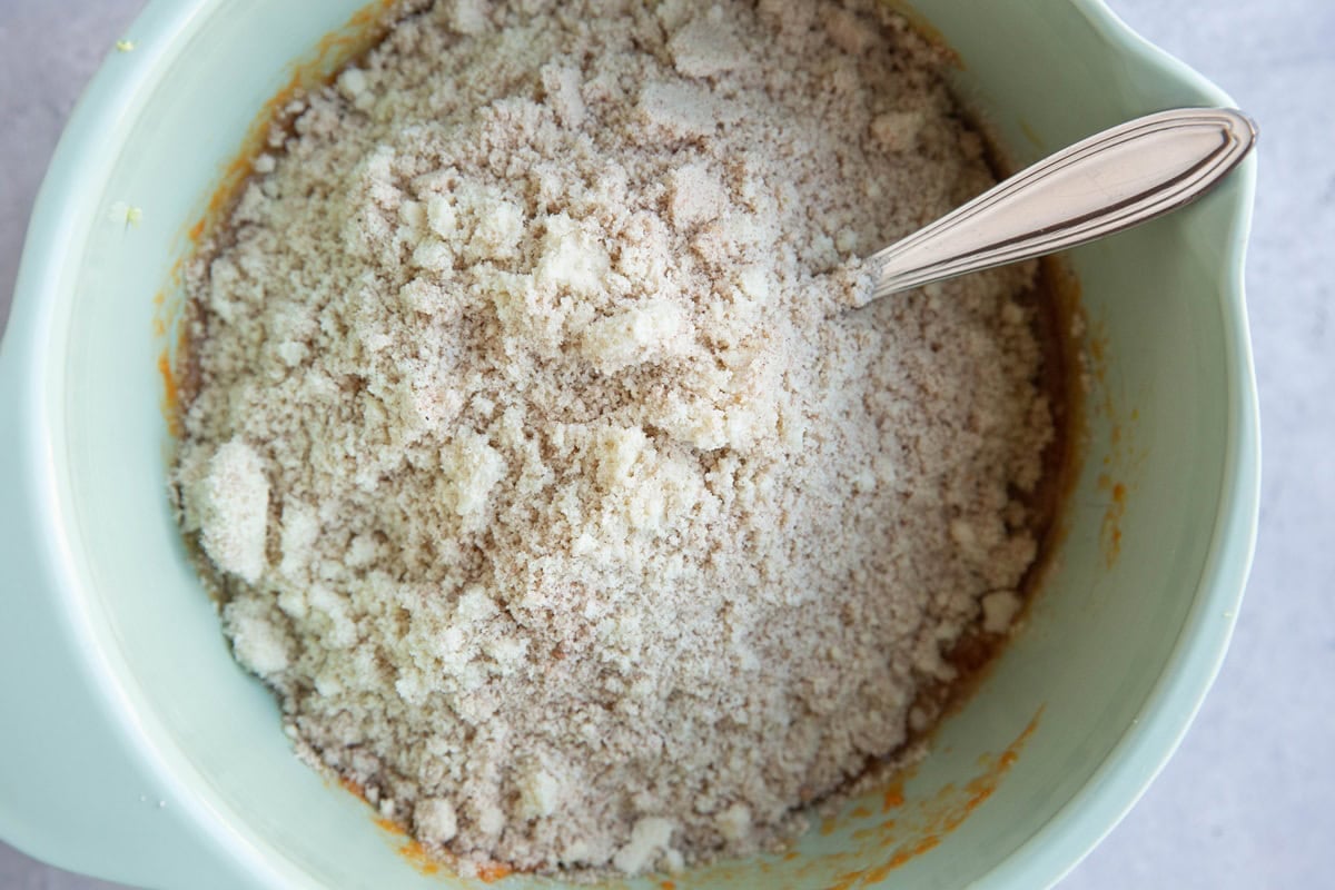 Mixing bowl full of wet ingredients with dry ingredients on top to make sweet potato muffins.