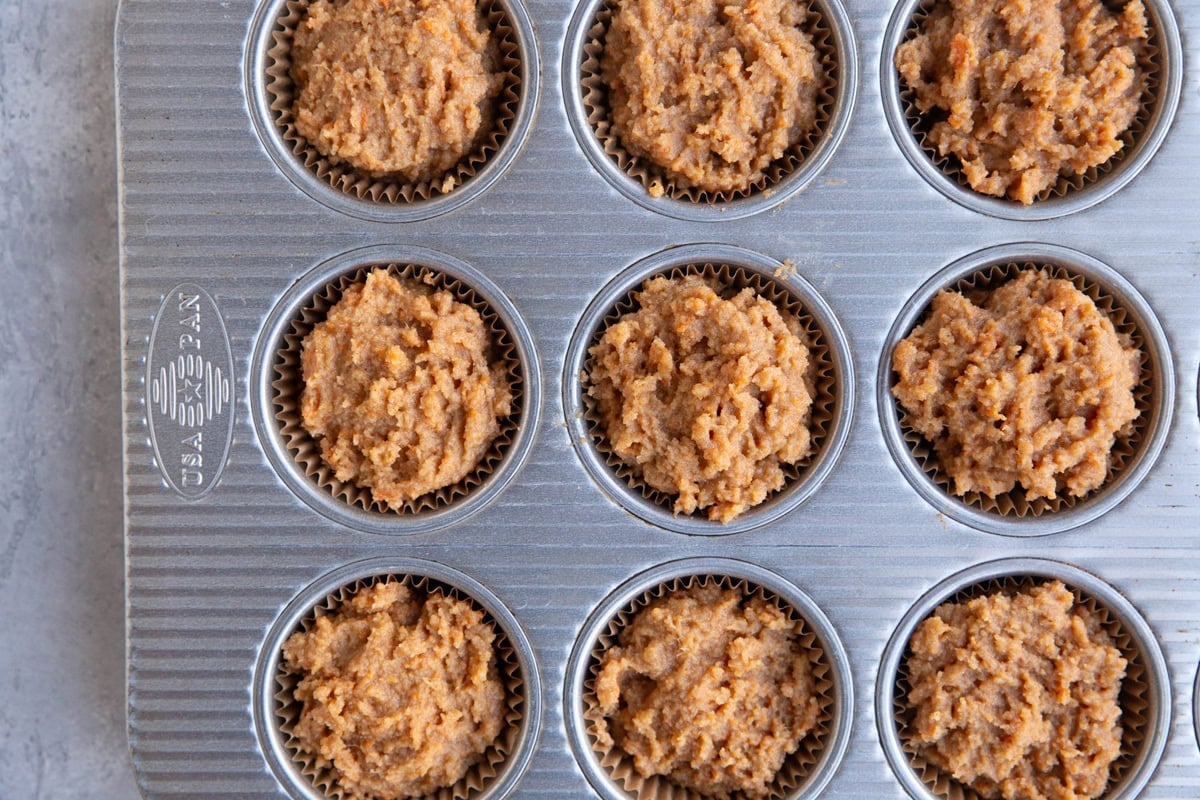 Sweet potato muffin batter in a muffin tin lined with paper liners, ready to go into the oven.