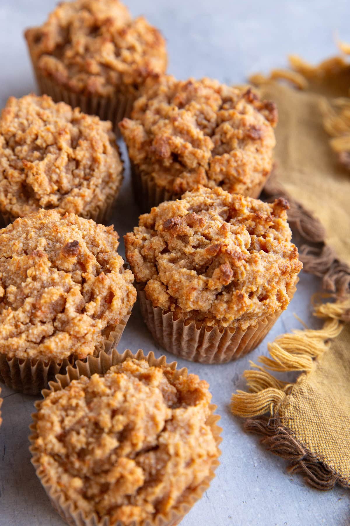 Six sweet potato muffins on a blue-grey surface with a golden napkin to the side, ready to eat.