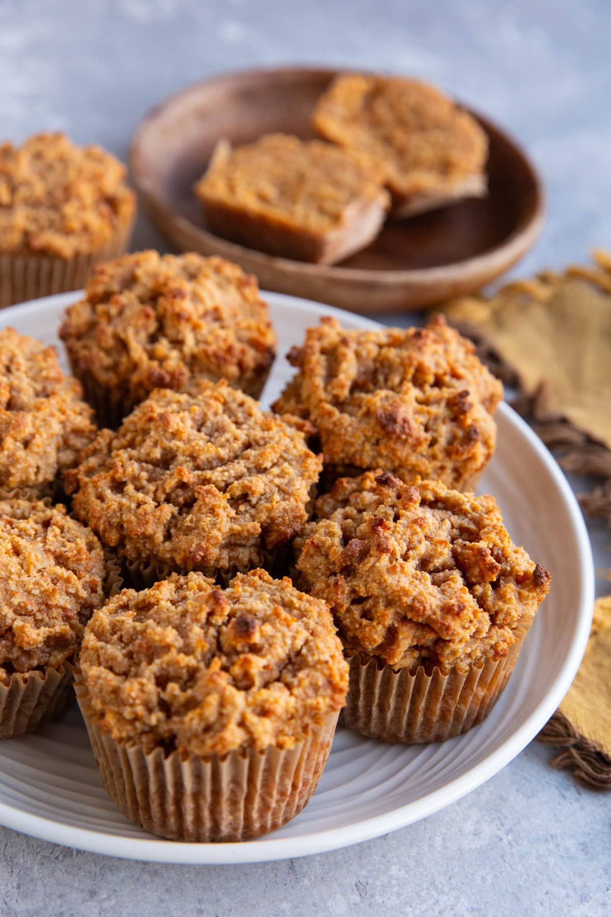 White plate of sweet potato muffins with a wooden plate with a sliced sweet potato muffin in the background.