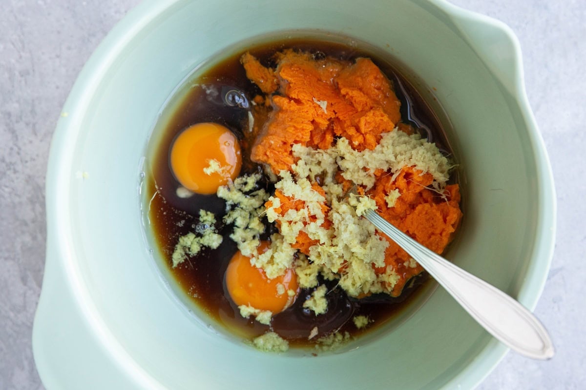 Mixing bowl full of mashed sweet potato, eggs, pure maple syrup, oil, and grated ginger.