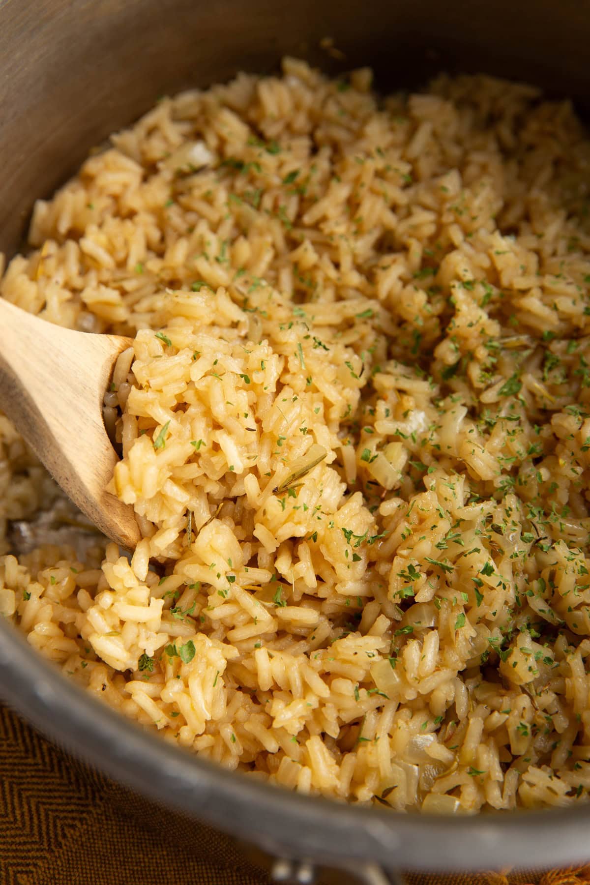 Chicken rice close up inside of a stainless steel pot with a wooden spoon inside to scoop the rice.