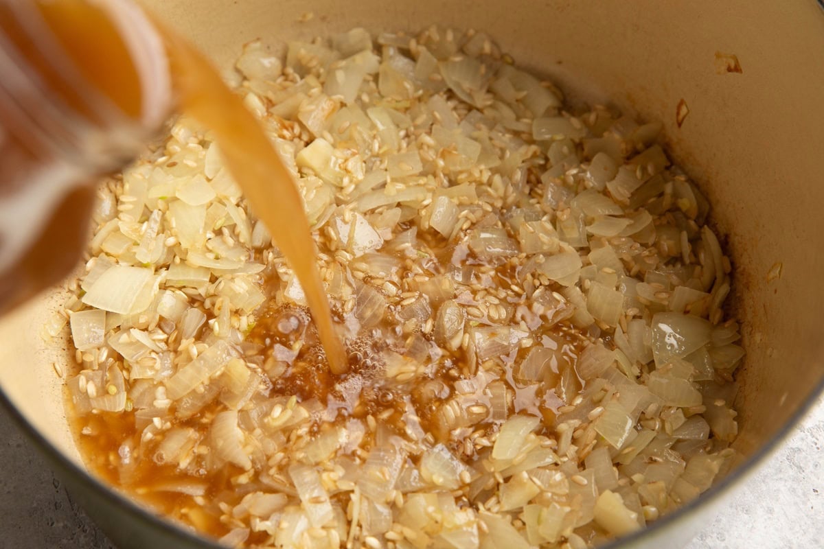 Pouring broth into a pot with onion and rice to make soup.