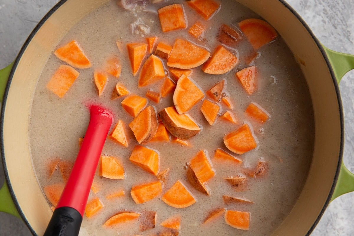 Creamy broth in a pot with chunks of sweet potato and a rubber spatula to stir it in.