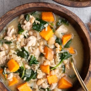 Two wooden bowls full of chicken and sweet potato soup with a gold spoon and a gold napkin to the side.