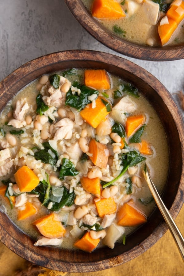 Two wooden bowls full of chicken and sweet potato soup with a gold spoon and a gold napkin to the side.