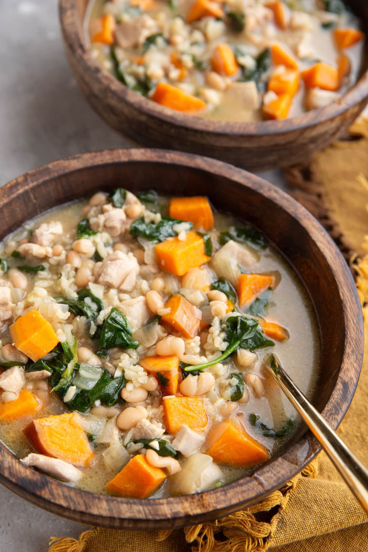 Two wooden bowls of chicken and sweet potato soup with a golden napkin to the side, ready to eat.