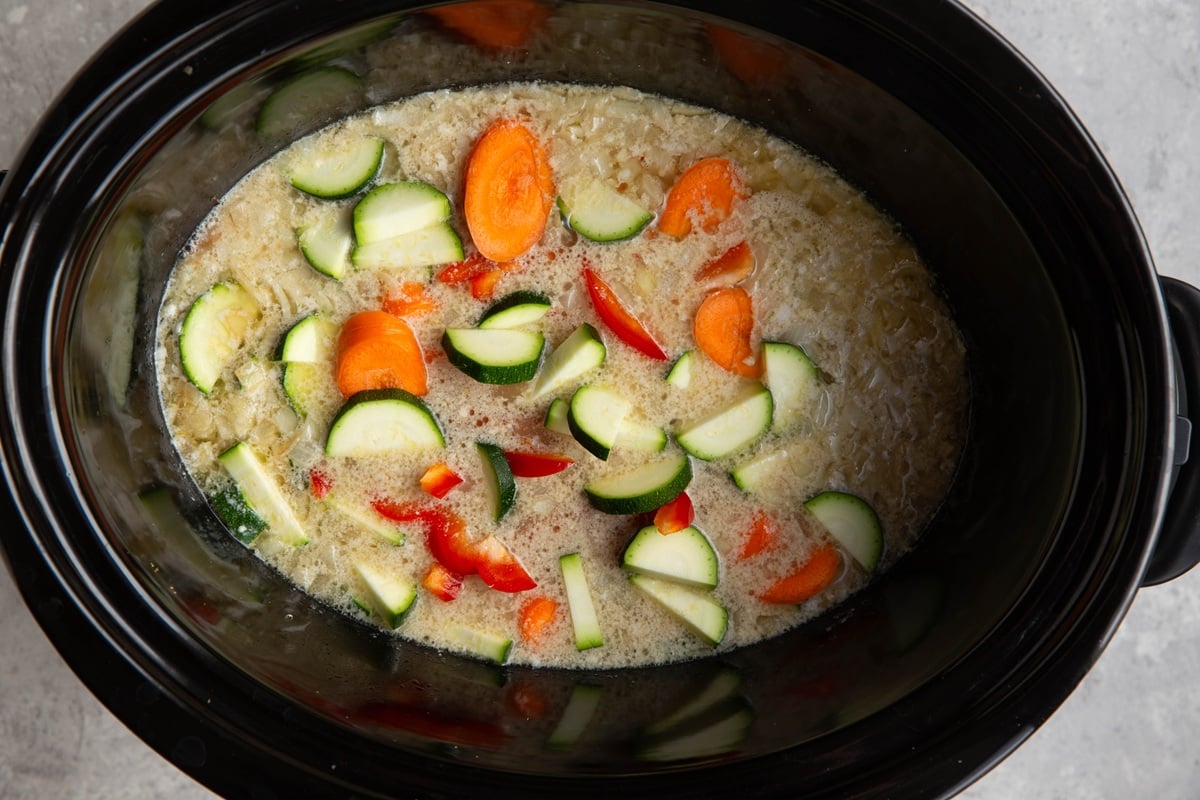 Crock pot with creamy soup inside and fresh vegetables having just been added in to continue cooking.
