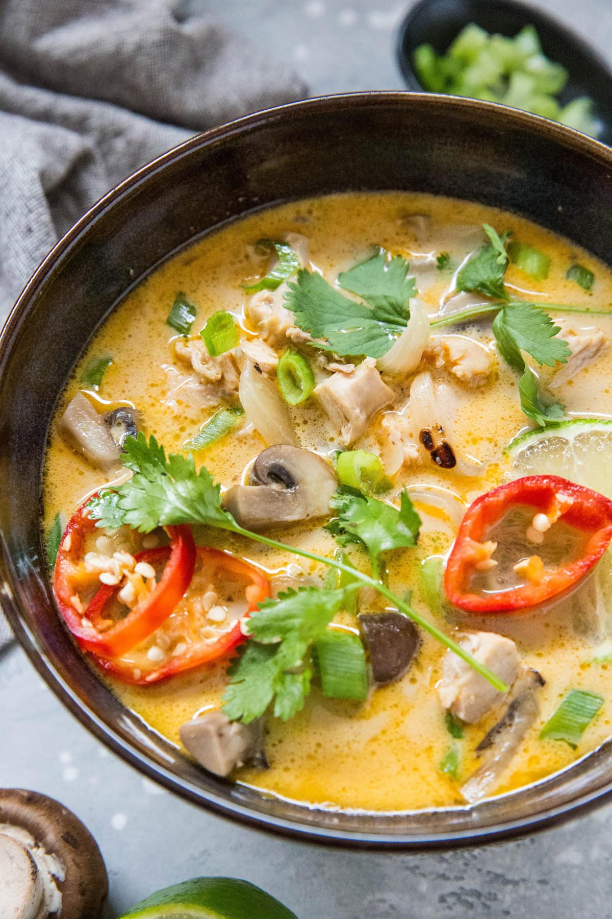 Coconut chicken soup in a bowl with visible chicken, mushrooms, cilantro and red chili peppers on top. Ready to serve.