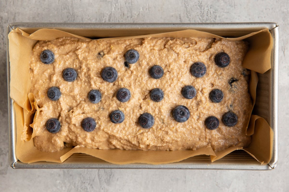 Loaf pan with bread batter and fresh blueberries sprinkled on top, ready to go into the oven.