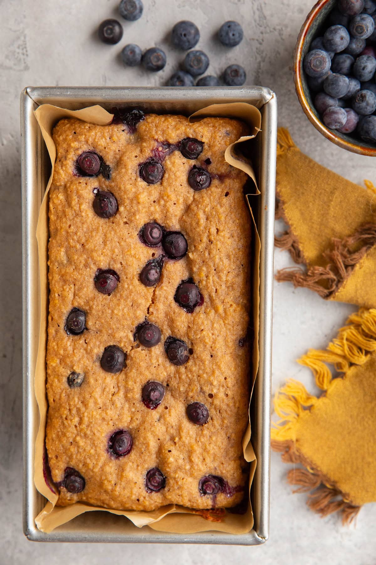 Loaf pan with yogurt blueberry bread and a small bowl of fresh blueberries to the side.