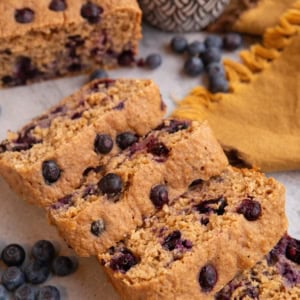 Loaf of blueberry oatmeal yogurt bread cut into slices with a bowl of fresh blueberries in the background.