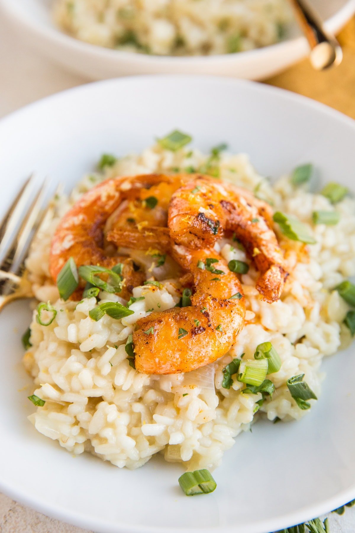 White plate with shrimp on top of risotto sprinkled with green onions.
