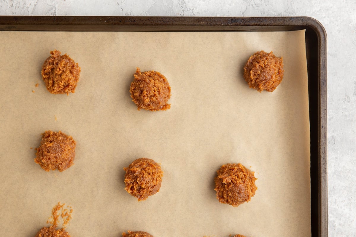 Cookie sheet lined with parchment paper with peanut butter cookie dough lumps, ready to go into the oven.