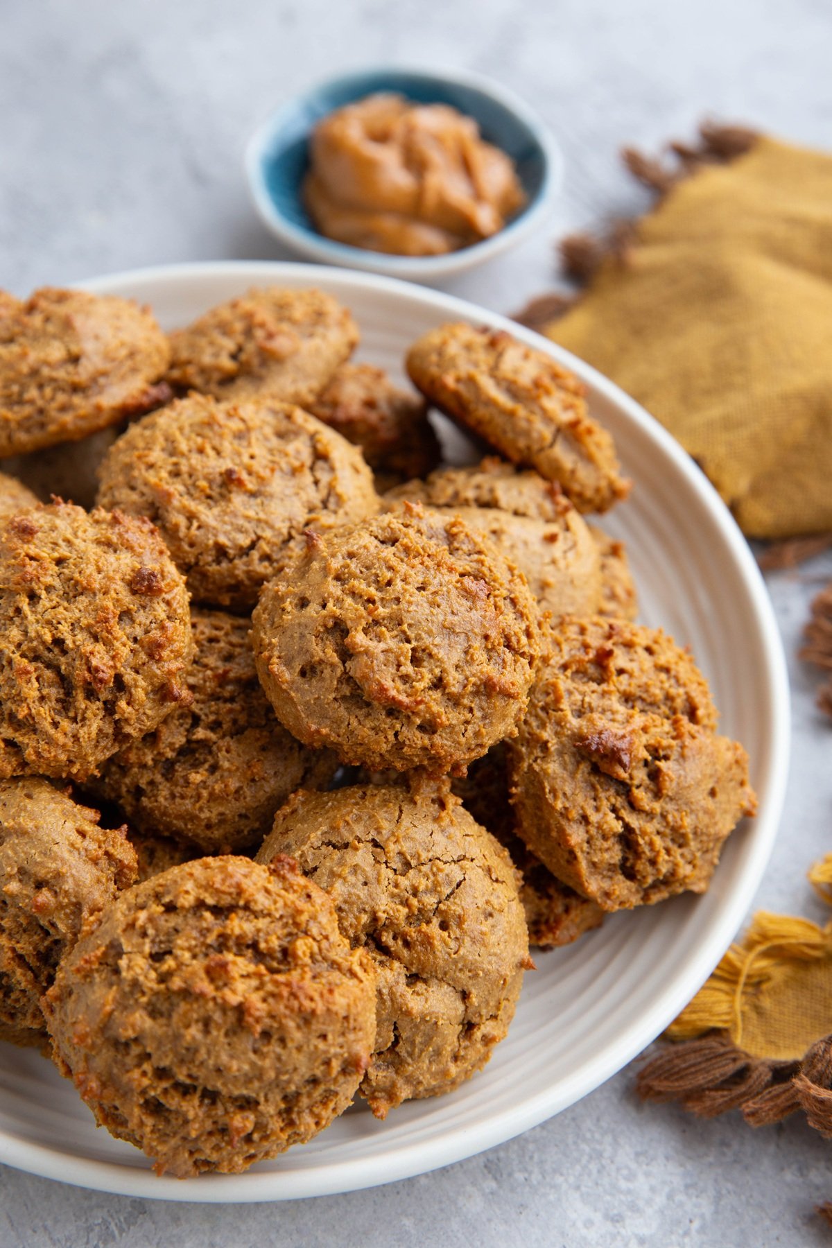 Plate of cottage cheese peanut butter cookies with a bowl of peanut butter in the background and a golden napkin to the side.