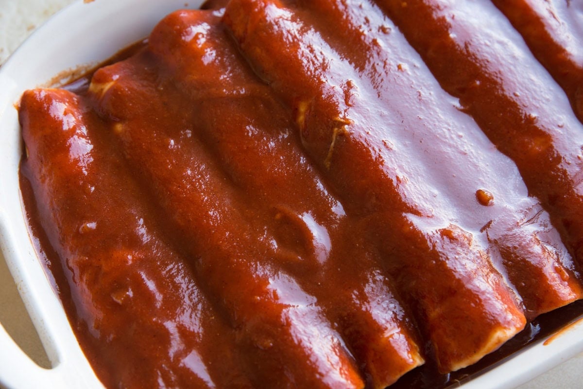 Prepared enchiladas in a baking dish with a lot of enchilada sauce spread on top.
