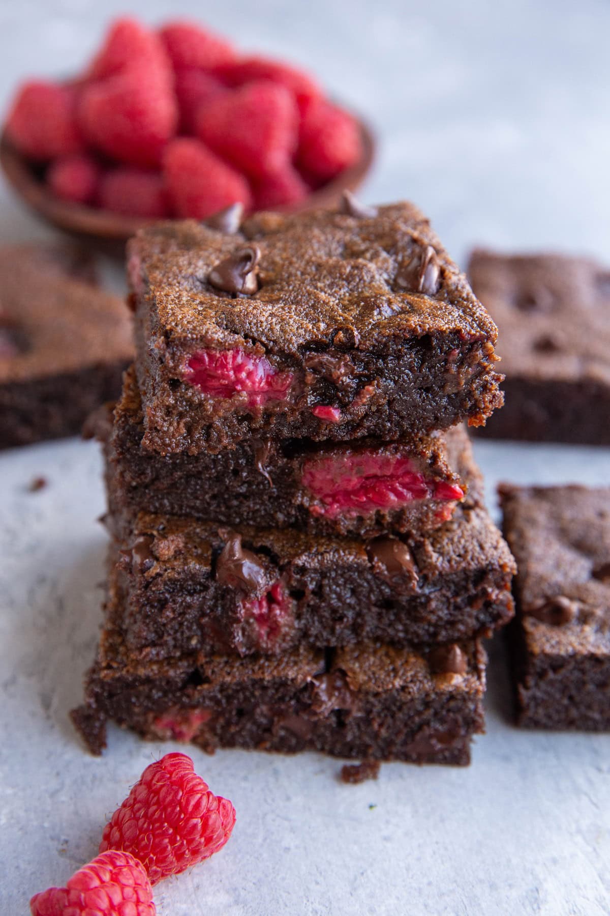 Stack of raspberry brownies with fresh raspberries in the background.