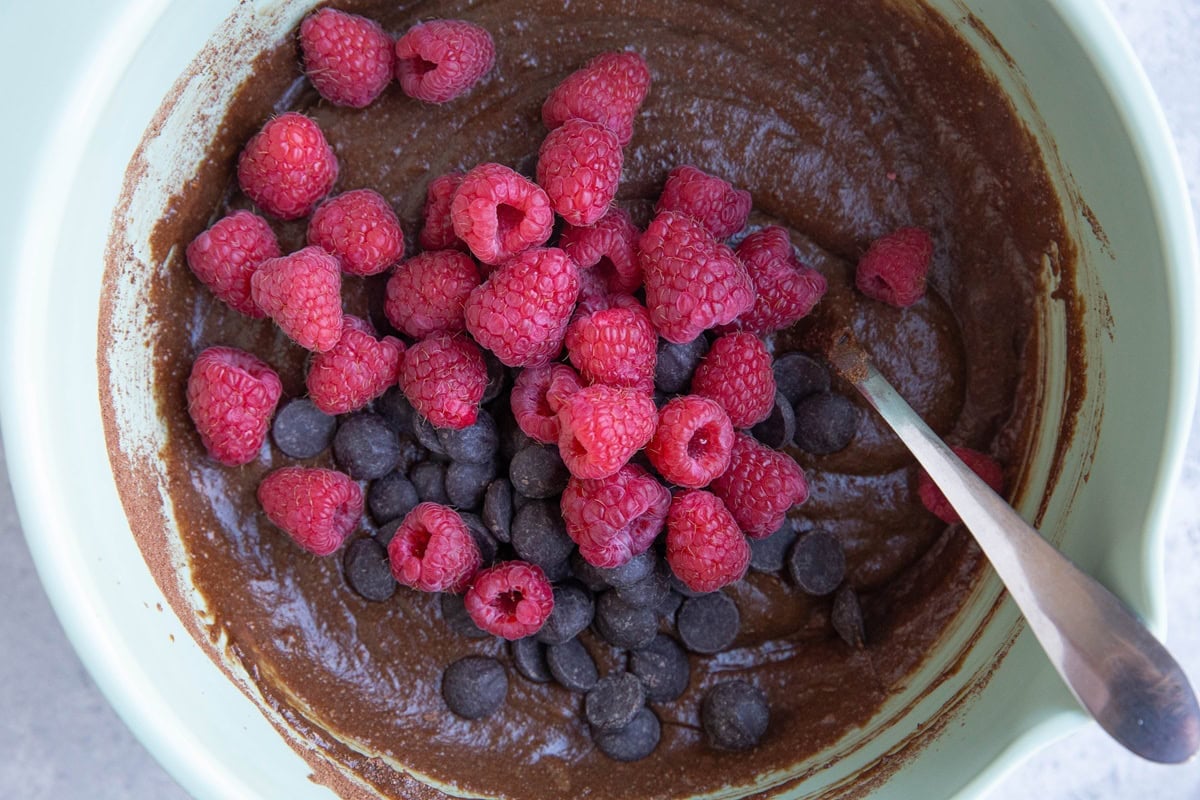 Mixing bowl full of brownie batter with chocolate chips and raspberries