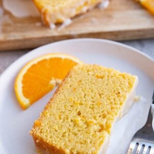Slice of orange pound cake on a white plate with the rest of the pound cake cut into slices in the background. Ready to serve.