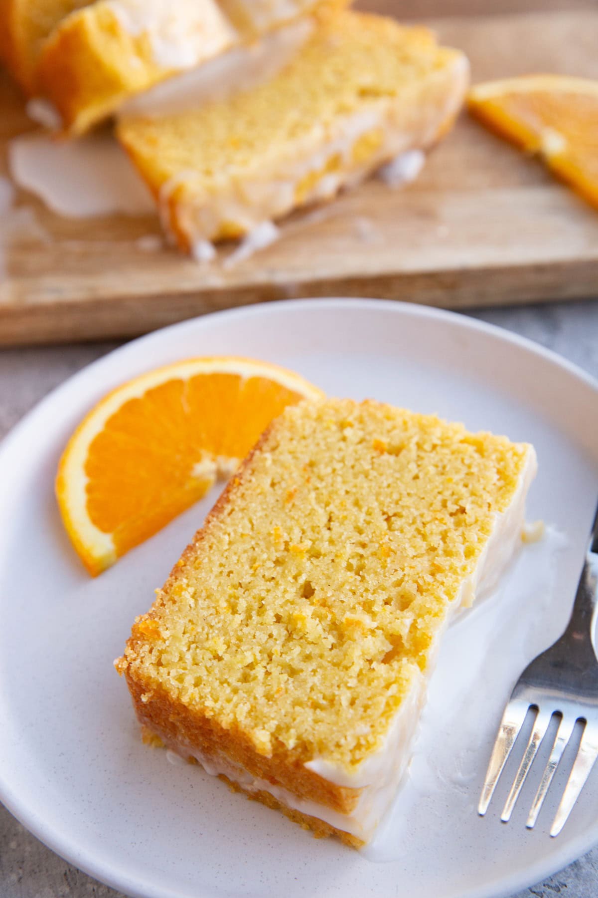 Slice of orange pound cake on a white plate with the rest of the pound cake cut into slices in the background. Ready to serve.