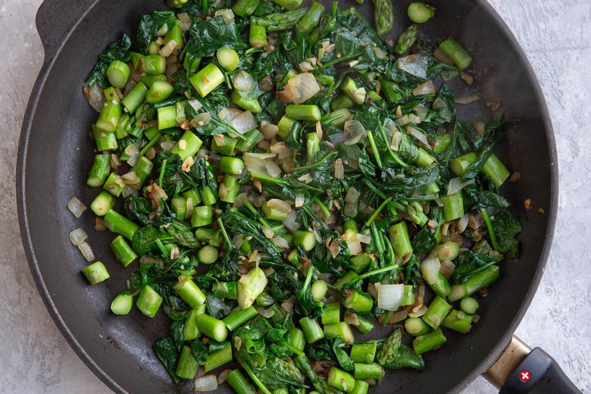 Nonstick skillet full of chopped asparagus, spinach, onion, and garlic.
