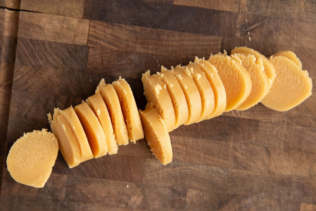 Wooden cutting board with almond paste cut into thin slices.