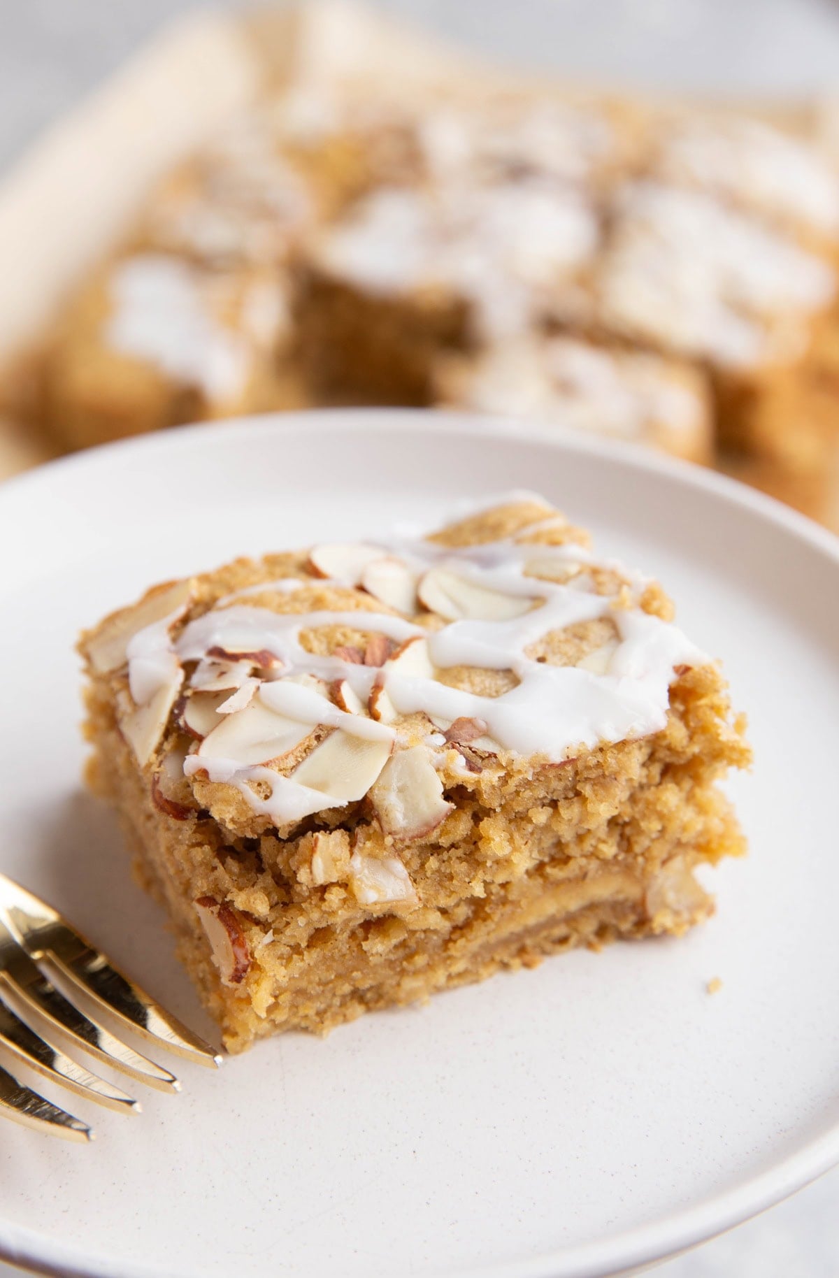 Slice of bear claw cake with a gold fork on a white plate with the rest of the cake in the background.