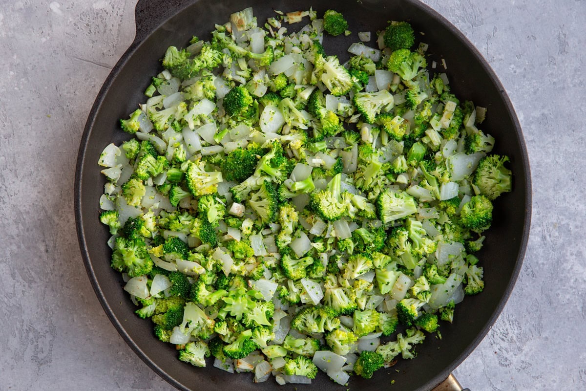 Large nonstick skillet with onions, garlic, and broccoli cooking.