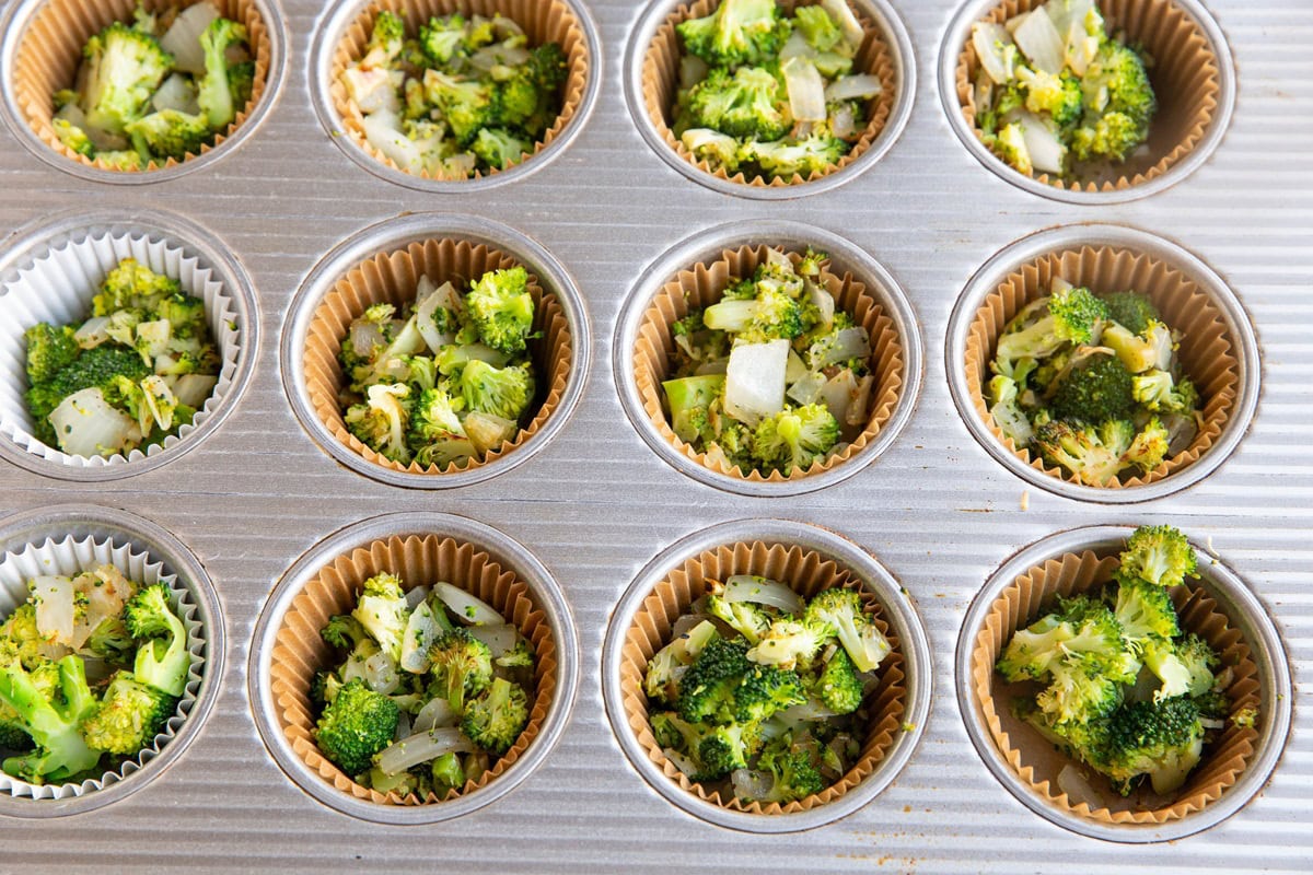 Muffin tray with paper liners filled with sauteed broccoli and onion.
