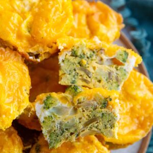 Plate of broccoli cheddar egg muffins with one sliced in half so you can see the inside.