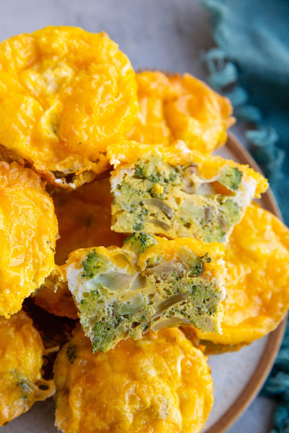 Plate of broccoli cheddar egg muffins with one sliced in half so you can see the inside.