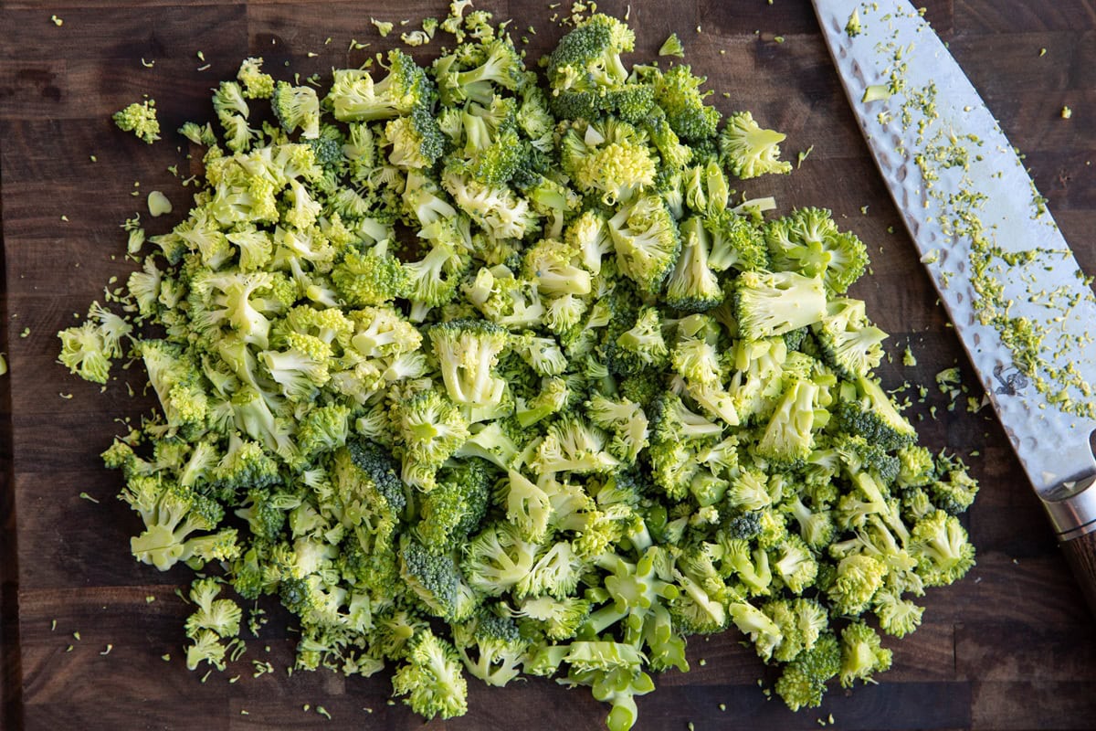 Chopped broccoli florets on a wooden cutting board, cut into small pieces.