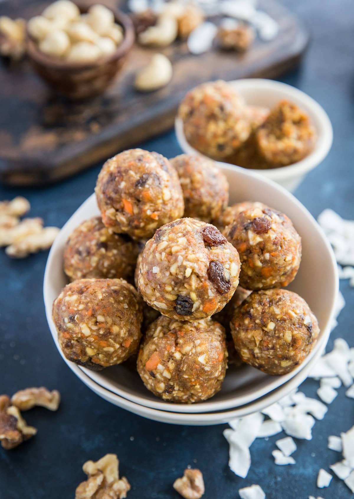 White bowls full of carrot cake energy bites with a smaller white bowl of more bites in the background and nuts and flaked coconut to the side.