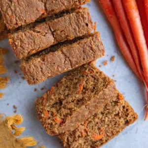 Carrot ginger cake cut into slices (in the form of a loaf) on a blue backdrop with fresh carrots and a golden napkin to the side. Ready to serve.