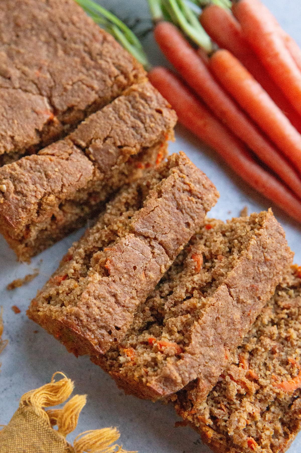 Loaf of carrot ginger cake cut into slices with fresh carrots in the background.