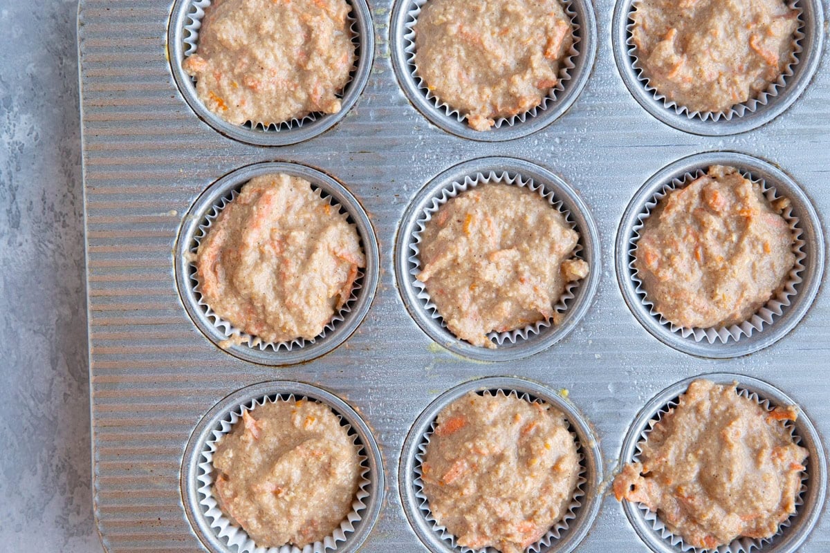 Carrot orange ginger muffin batter in a muffin tray, ready to go into the oven.
